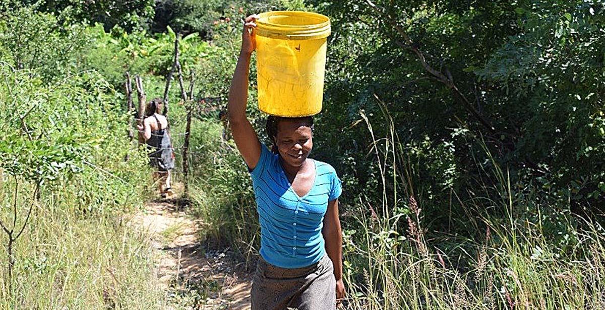 Takudzwa (a national volunteer) bringing water up from the Odzi River to water the garden