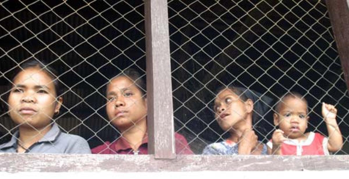 Women look through a wire screen at a window in Timor-Leste